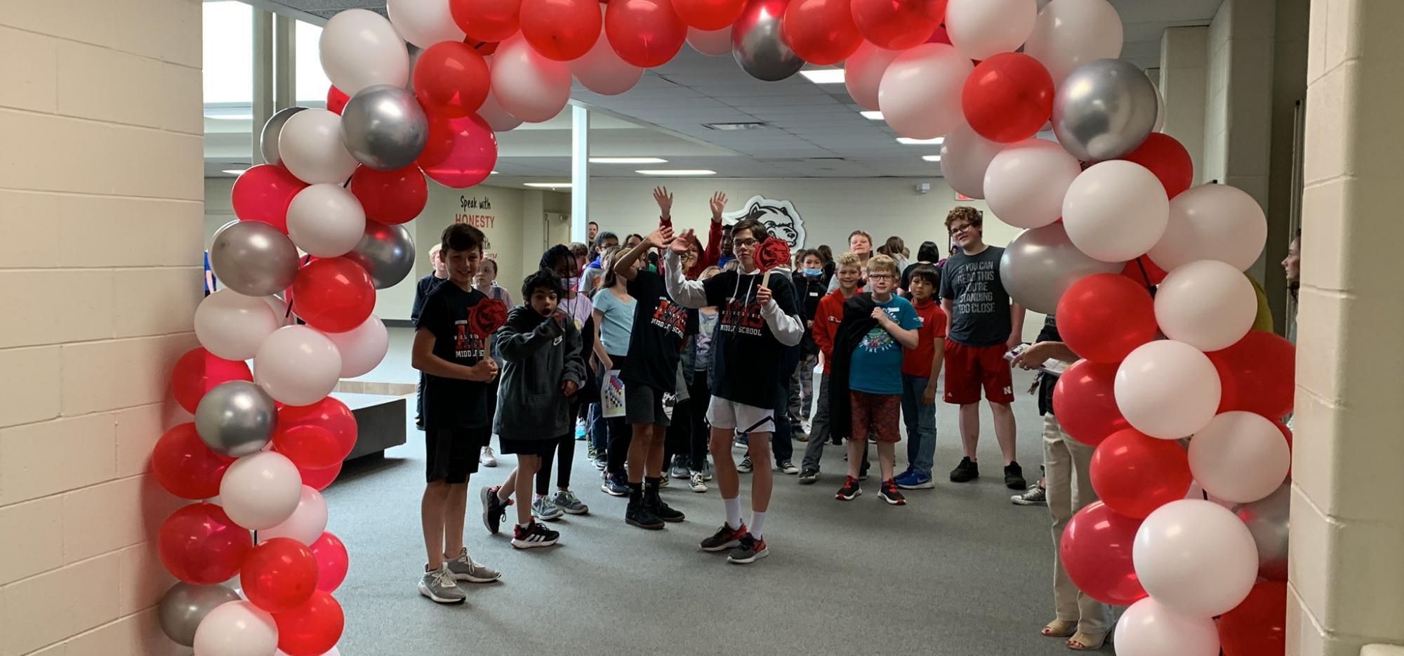 Red and white balloon arch with students greeting